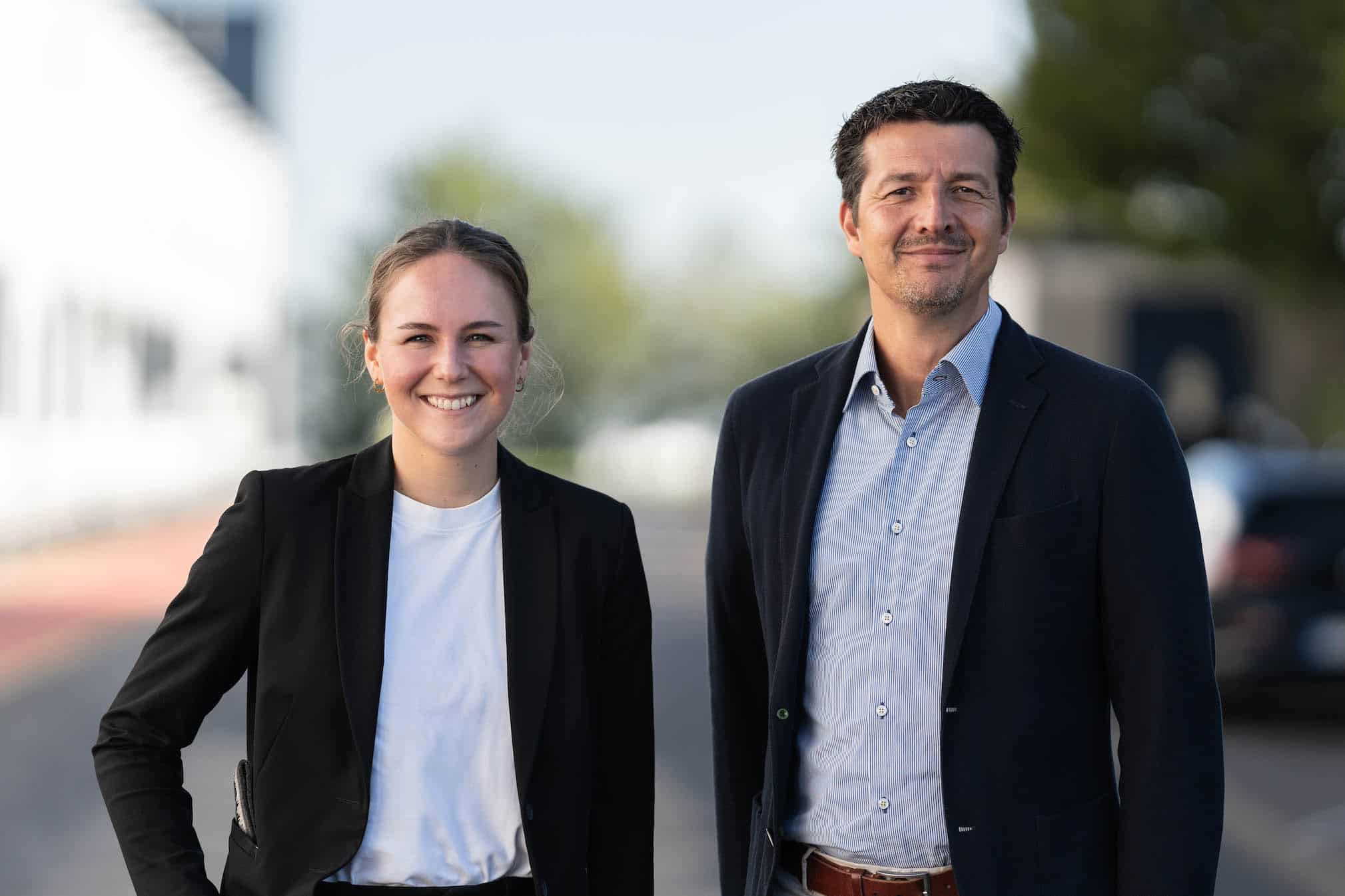 Dwóch CLASSEN w strojach biznesowych stoi na zewnątrz i uśmiecha się do aparatu – symbol profesjonalizmu, ducha zespołowego i kompetencji w firmie.