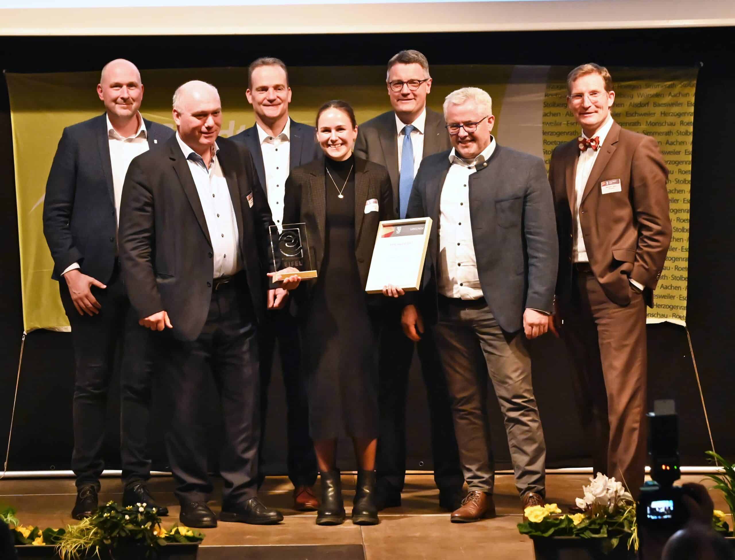 Zdjęcie grupowe z ceremonii wręczenia nagród: kilka osób stoi na scenie, kobieta trzyma w rękach nagrodę i dyplom – symbol sukcesu, uznania i doskonałych osiągnięć CLASSEN .