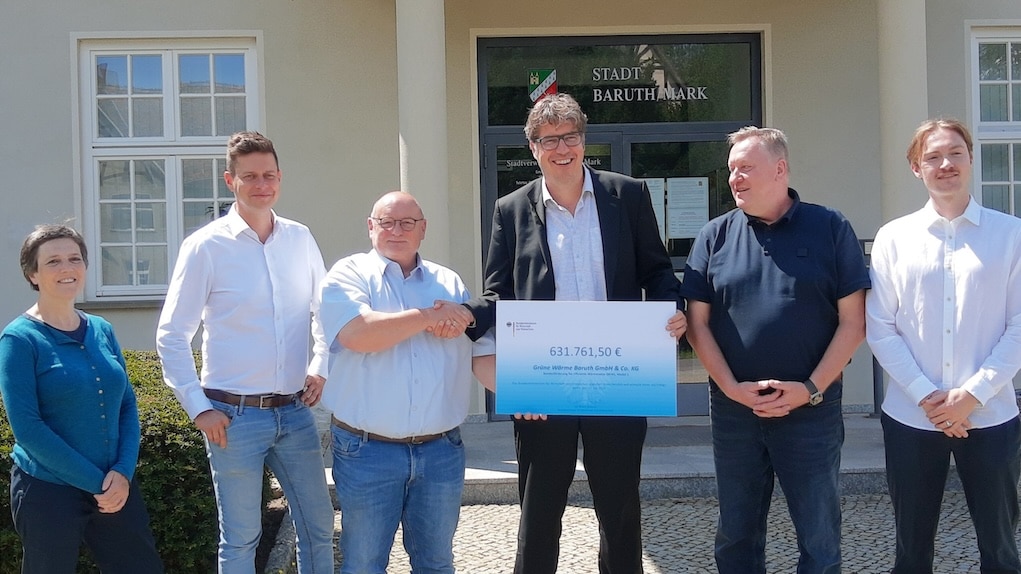 Oficjalne przekazanie certyfikatu finansowania na kwotę 631 761,50 EUR przed ratuszem w Baruth/Mark: kilka osób pozuje razem z czekiem - symbolem wsparcia dla projektów zrównoważonej energii i współpracy regionalnej.