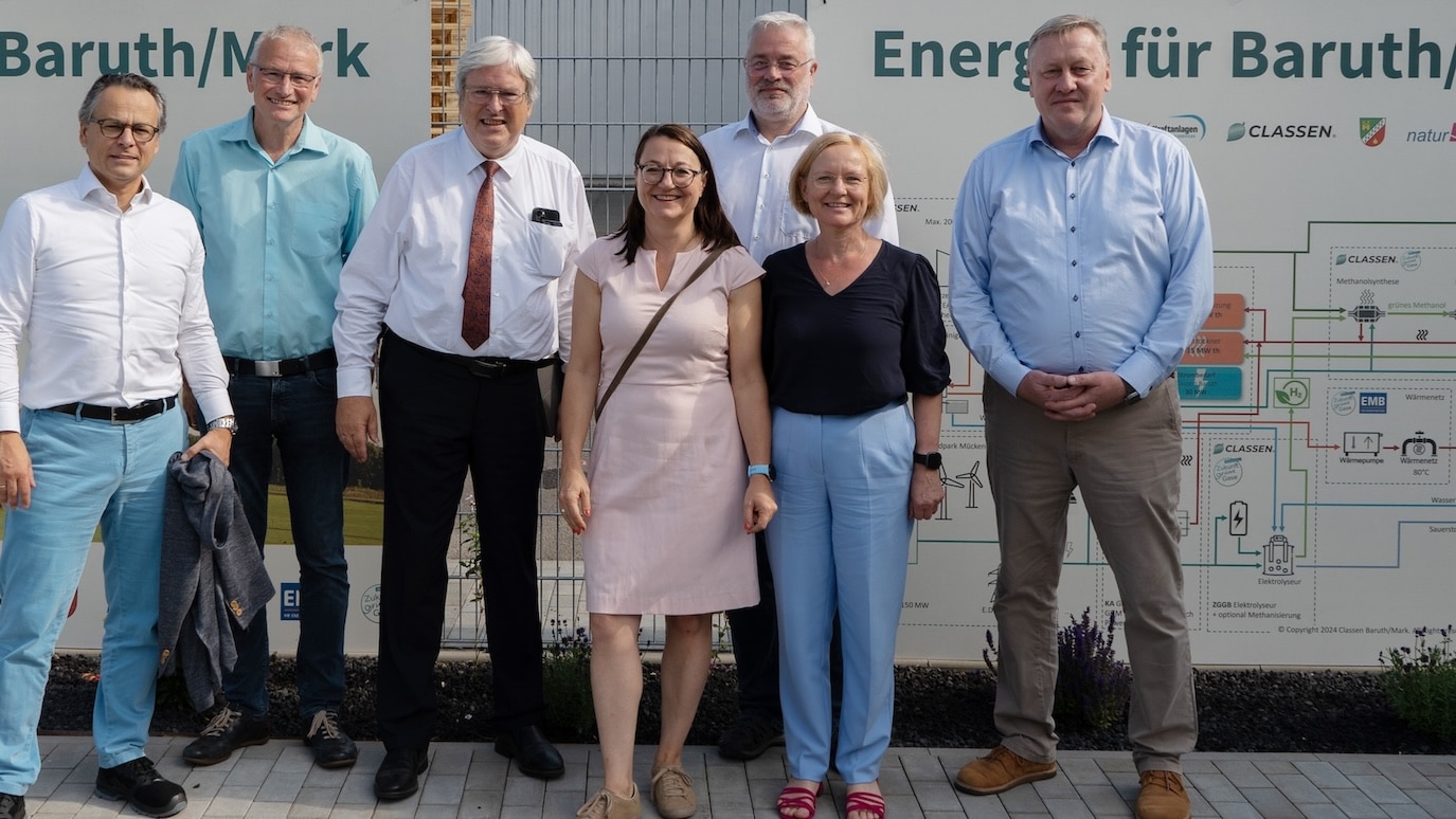 Grupa siedmiu osób przed tablicą informacyjną w CLASSEN w Baruth/Mark, zdjęcie wykonane podczas oficjalnej wizyty – symbol wymiany, współpracy i zrównoważonych projektów energetycznych.