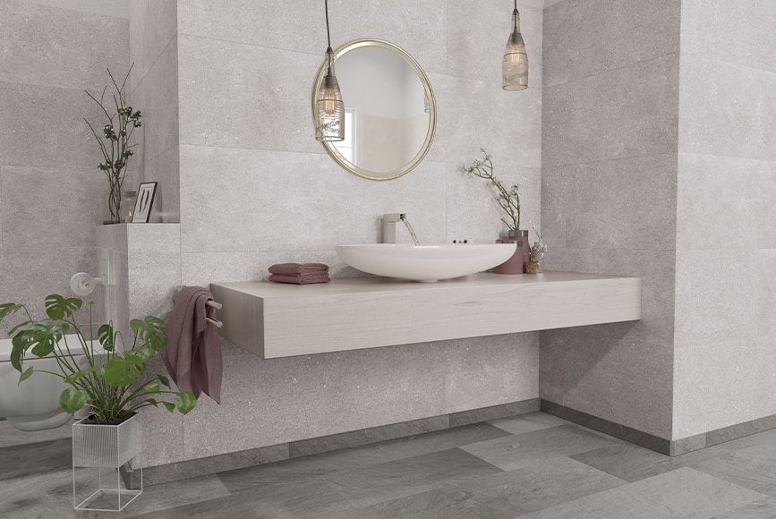 Łazienka z szarymi płytkami i okrągłym lustrem nad umywalką