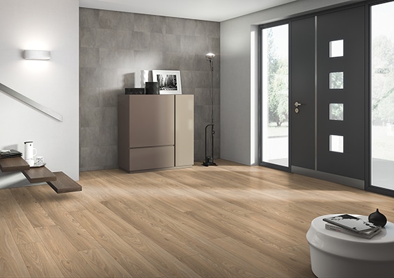 Nowoczesna strefa wejściowa z jasną podłogą winylową imitującą drewno, szarymi drzwiami wejściowymi i minimalistycznym wyposażeniem.