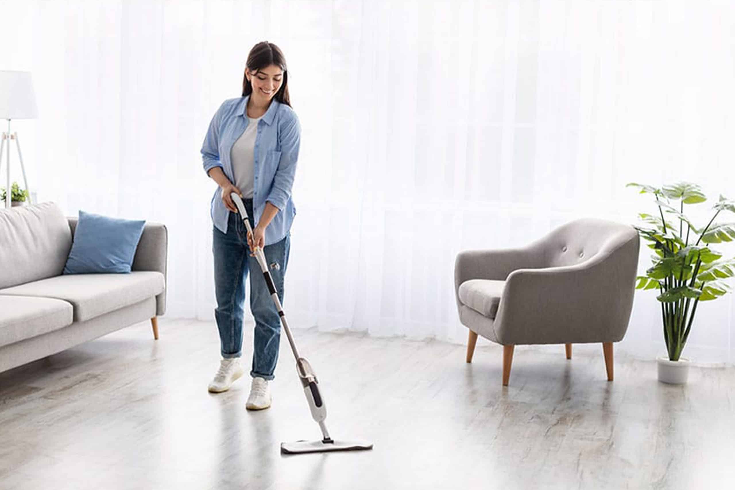 Młoda kobieta myje jasną podłogę w nowoczesnym salonie - łatwa w pielęgnacji, wytrzymała wykładzina podłogowa o wyglądzie drewna.