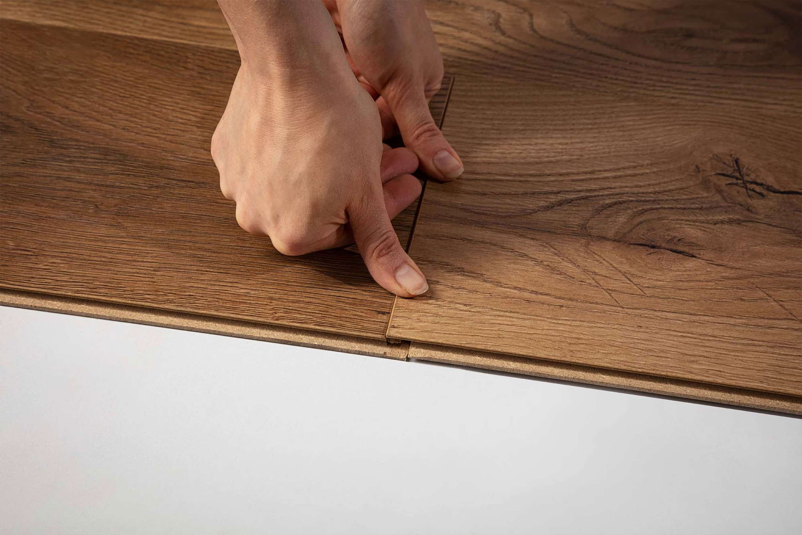 Zbliżenie rąk układających brązowe deski laminowane z systemem zatrzaskowym - prosta podłoga drewnopodobna.