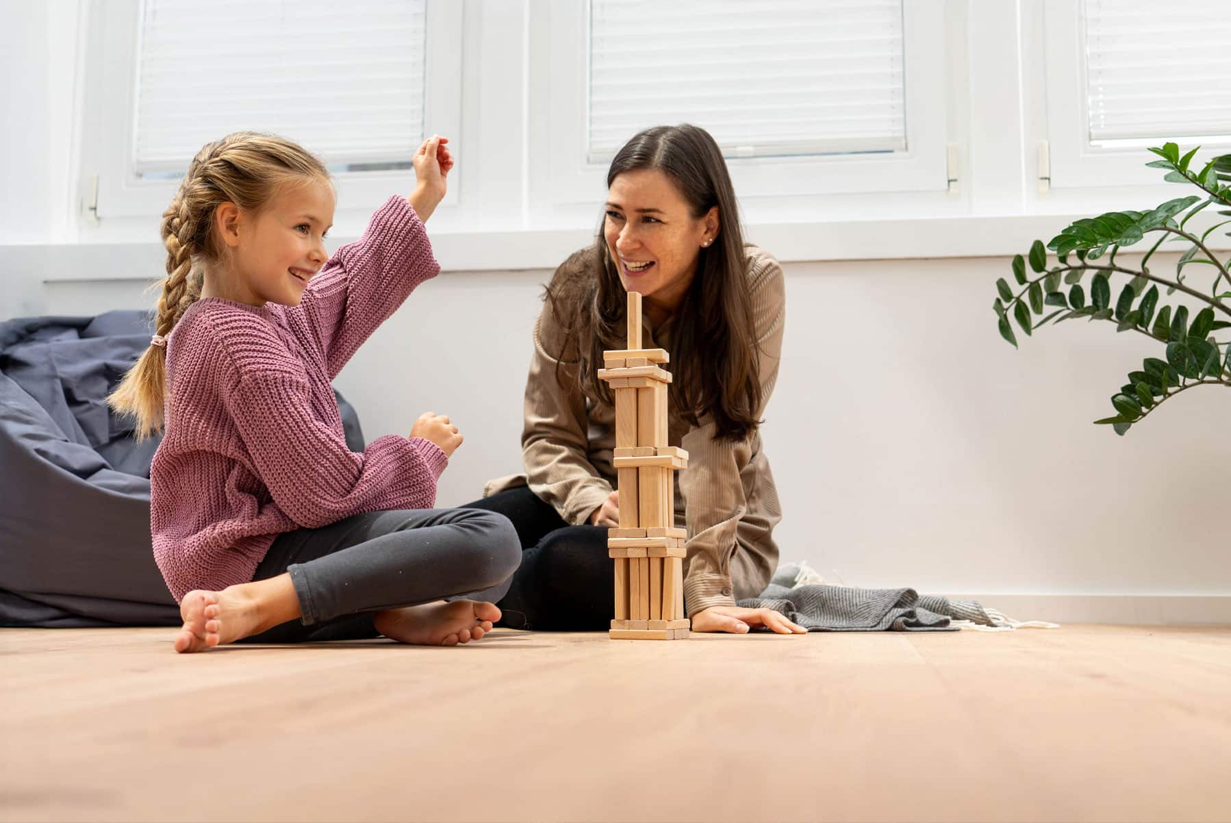 Kobieta i dziecko siedzą na podłodze i budują wieżę.